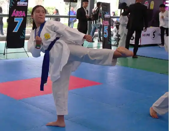 Joven practicando patada lateral con uniforme y cinturón azul en clases de Taekwondo en Lobos TKD Pachuca